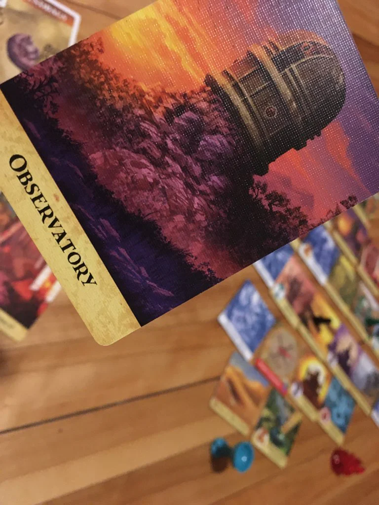 Observatory Card in the foreground with the game board in the background on a wooden table.